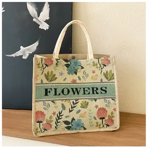 Detail of floral embroidery on beige linen tote bag with magnetic clasp and FLOWERS text