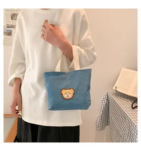 Detailed close-up of blue corduroy tote bag with brown bear embroidery and cream handles