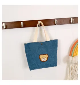 Detail of blue corduroy handbag featuring a plush bear patch and snap button closure