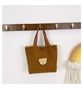 Detail of a brown corduroy handbag featuring a cute bear embroidery on a wooden hook