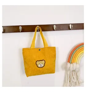 Detail of yellow corduroy handbag featuring a 3D teddy bear patch and metal snap closure