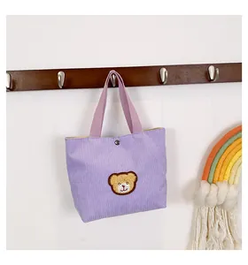 Detail of purple corduroy tote bag with plush bear patch and silver snap button closure