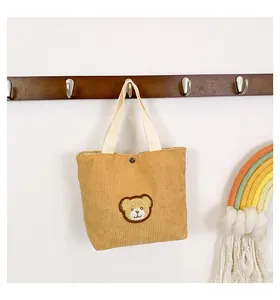 Close-up of yellow corduroy tote bag featuring a cute embroidered bear and metal snap button