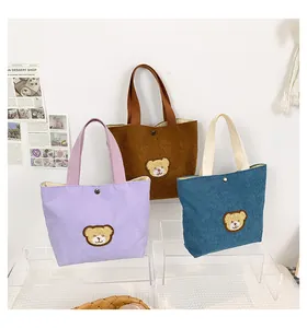 Detailed corduroy tote bag showing metal button closure and plush bear embroidery