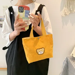 Cute bright yellow corduroy handbag featuring a plush bear patch and snap closure