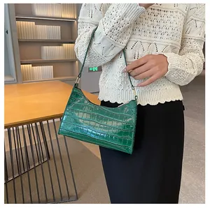 Model draagt een groene baguette tas met krokodillenreliëf en glanzende lakleren afwerking