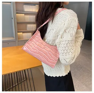 Detail van roze baguette tas met krokodillenreliëf gedragen door een model in een interieur