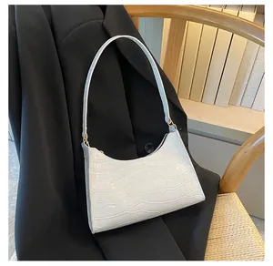 Close-up van witte hobo-tas met krokodillenpatroon op een zwarte blazer en gouden details