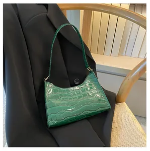 Detail van donkergroene krokodillentextuur op een laklederen baguette-tas op een blazer