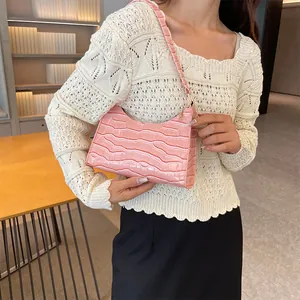 Roze onderarmtas met krokodillenprint gedragen door een model in een elegante omgeving