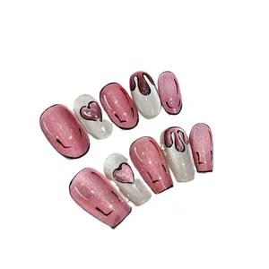 Pink glitter cat-eye press-on nails with black hand-drawn art and heart patterns