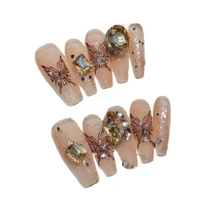 Handmade press-on nails in nude pink with butterfly patterns and amber rhinestones