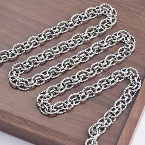 Detail of silver stainless steel chain with textured diamond pattern on wooden base