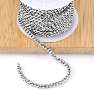 Polished silver stainless steel Cuban link chain roll on white plastic spool with wood background