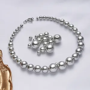 Collana di perle grigie sfumate e perle di vetro sfuse su sfondo in tessuto bianco