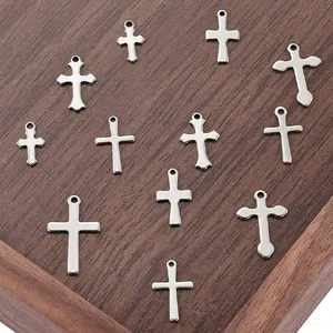 Assorted polished stainless steel cross pendants on a rustic wooden tray for DIY jewelry