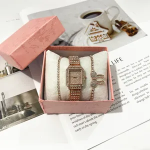 Nahaufnahme einer roségoldenen quadratischen Damenuhr und Armbändern in rosa Geschenkbox