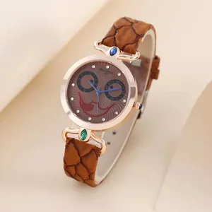 Detail of rose gold watch dial with rhinestone owl face and jewel-set lugs on brown strap