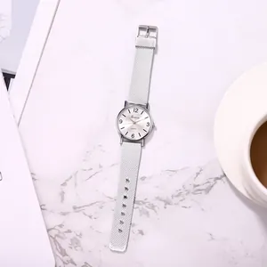 Geneva silver quartz watch with mesh strap on marble surface next to coffee cup