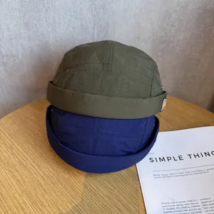Army green and navy blue nylon ripstop dockers caps on a wooden table with magazine