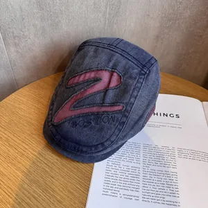 Close-up of vintage blue denim flat cap with red Z patch embroidery on a wooden table
