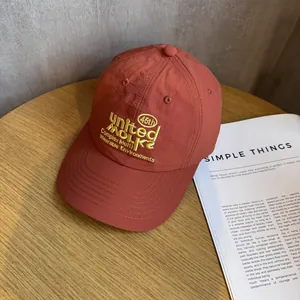 Detail einer ziegelroten Nylon-Baseballkappe mit gelber Stickerei auf einem Holztisch