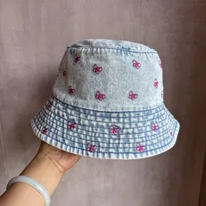 Détail de la broderie de papillon rose sur la matière denim bleu clair du chapeau cloche