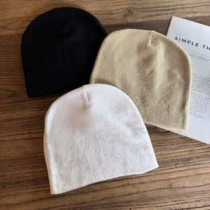 Dettaglio di berretti in maglia minimalisti in nero, beige e bianco su fondo di legno