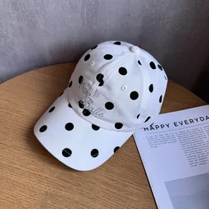 Detail view of a white polka dot baseball cap featuring Ciao Belle embroidery on a desk