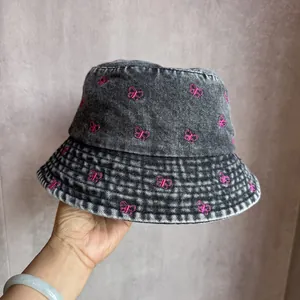 Gros plan sur la broderie papillon rose d'un chapeau bob en denim gris délavé