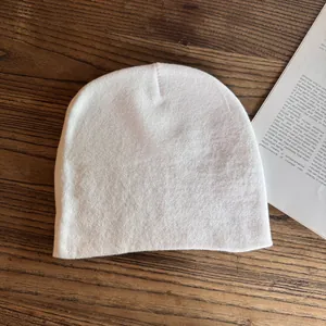 Berretto in maglia bianca su superficie di legno accanto a un libro per stile invernale