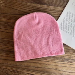 Vista piatta del berretto in maglia rosa su legno con libro mostra trama morbida