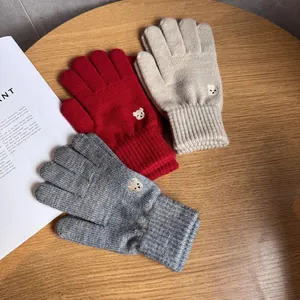 Close-up of knit gloves with bear embroidery in red, beige, and gray on wooden background