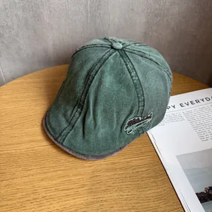 Close-up of retro green washed denim flat cap with red embroidery on wooden surface