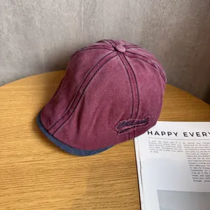Detail view of burgundy washed cotton flat cap with navy blue embroidery on wooden desk