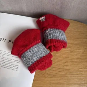 Close-up of red and grey knitted gloves featuring cute bear embroidery on a desk