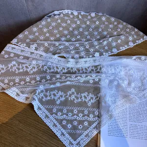 Weißer Spitzenschal mit hohlen Blumenmustern auf einem rustikalen Holztisch