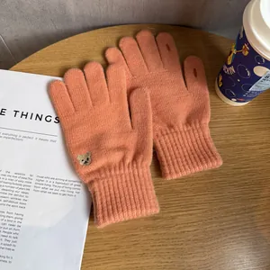 Close-up of orange knit gloves with cute bear embroidery on a rustic wooden table
