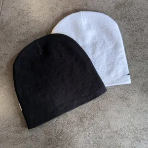 Flat lay detail of black and white jacquard knit beanies on stone texture background