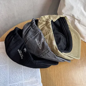 Three minimalist newsboy hats in black, grey, and khaki on a vintage wooden surface