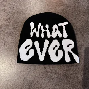 Close-up of black knit beanie featuring white jacquard WHATEVER graffiti lettering