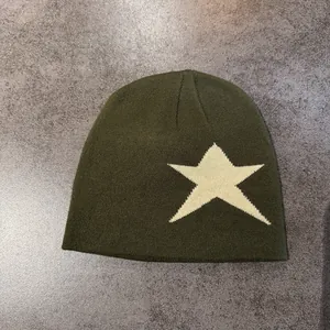 Détail du bonnet en maille vert olive avec une étoile blanche sur fond gris mat