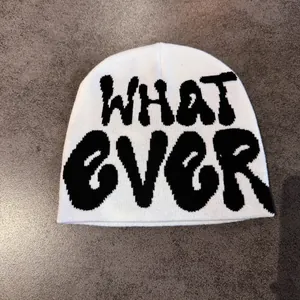 Close-up of white knitted beanie with black WHAT EVER jacquard lettering and thick texture
