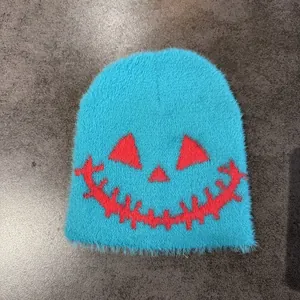 Detailed shot of soft teal faux mink knitted beanie with Halloween pumpkin face design