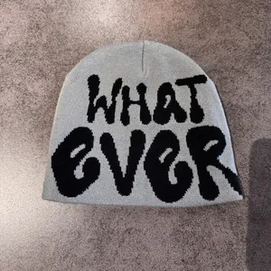 Detail of grey knitted beanie featuring black graffiti WHAT EVER jacquard lettering