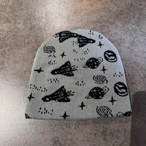 Detail van grijze gebreide muts met zwarte jacquardpatronen van raketten en planeten in de ruimte