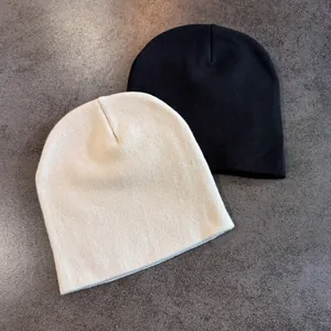 Detailed view of cream and black knitted beanies with fine ribbed texture on stone background