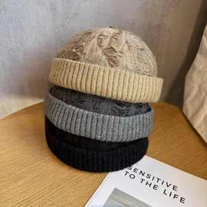 Close-up of stacked distressed knit skull caps in khaki, gray and black colors