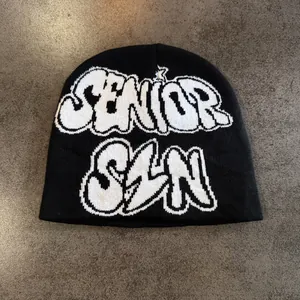 Gros plan d'un bonnet en tricot noir avec lettrage graffiti Senior Szn en blanc
