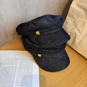 Navy blue striped corduroy newsboy caps with gold buttons on light wood background